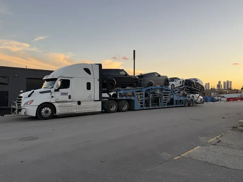 Fully loaded Snowbirds Auto Connection Freightliner and car carrier with city towers in the distance