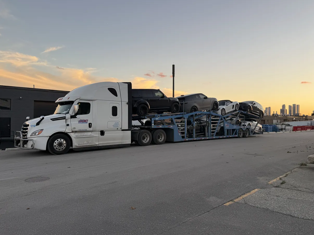 Fully loaded Snowbirds Auto Connection car carrier in Ontario Fully loaded Snowbirds Auto Connection Freightliner and car carrier with city towers in the distance